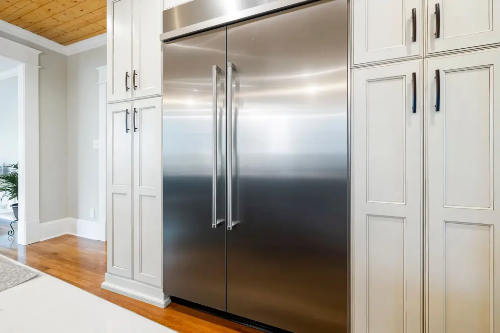 A stainless steel refrigerator between white kitchen cabinets